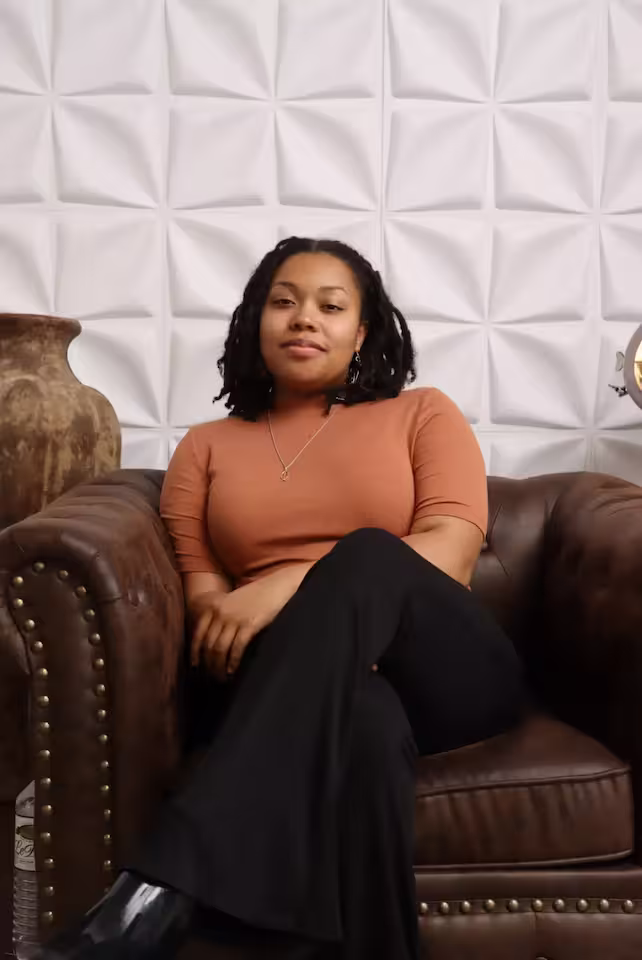 Confident Black woman with shoulder-length locs sitting on a brown leather armchair, smiling, representing SEO blog writing services.
